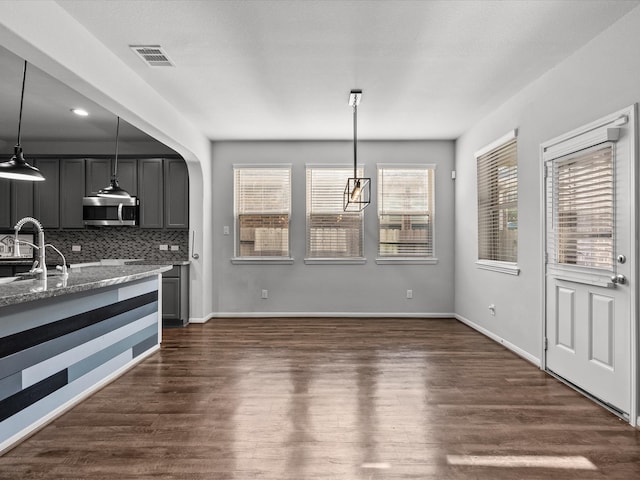 kitchen with decorative backsplash, dark hardwood / wood-style flooring, light stone counters, and hanging light fixtures