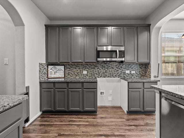 kitchen featuring gray cabinetry, backsplash, dark wood-type flooring, light stone counters, and stainless steel appliances