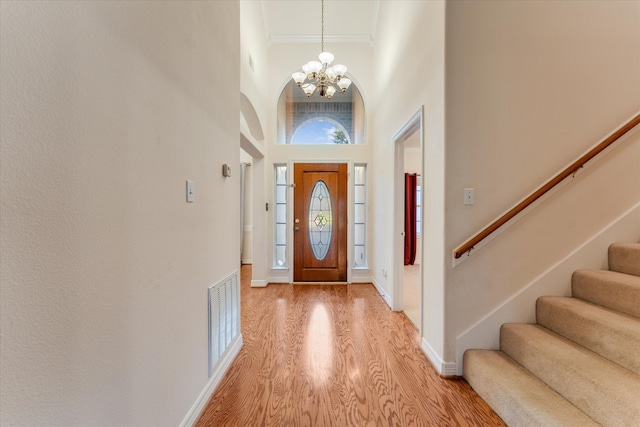 entryway with a chandelier, a high ceiling, light hardwood / wood-style flooring, and ornamental molding