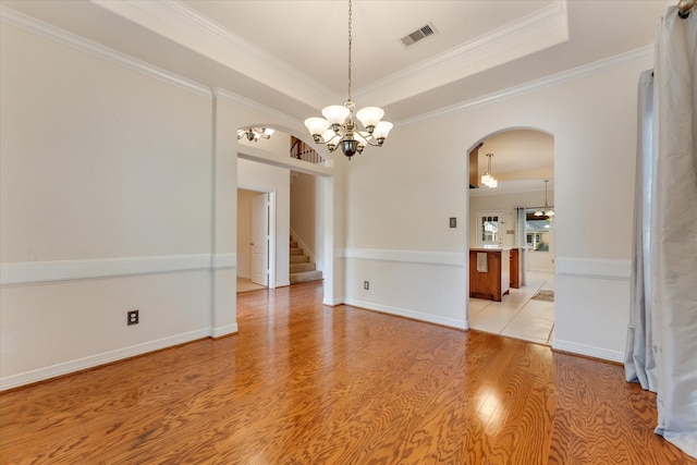 spare room featuring a tray ceiling, an inviting chandelier, ornamental molding, and light wood-type flooring