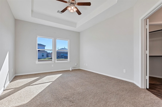 unfurnished bedroom with a walk in closet, carpet flooring, ceiling fan, a tray ceiling, and a closet