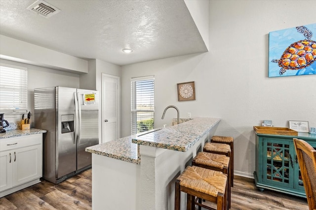 kitchen with stainless steel refrigerator with ice dispenser, dark hardwood / wood-style flooring, light stone counters, a breakfast bar, and white cabinets