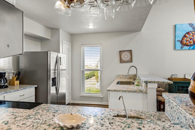 kitchen featuring light stone countertops, a textured ceiling, sink, stainless steel fridge with ice dispenser, and white cabinetry