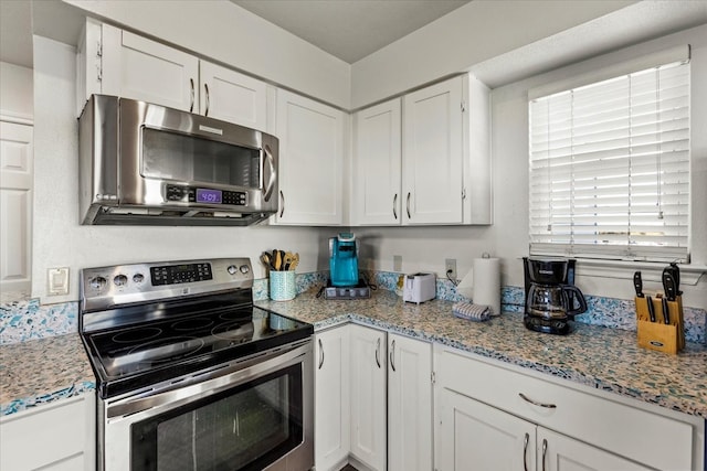 kitchen with appliances with stainless steel finishes, white cabinetry, and light stone counters