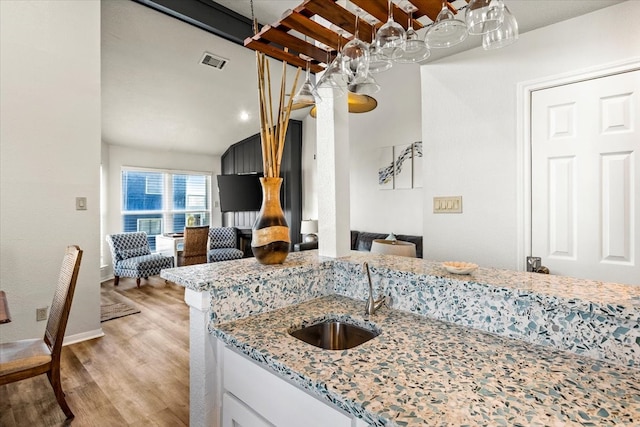 kitchen with light stone countertops, white cabinetry, sink, and light hardwood / wood-style flooring