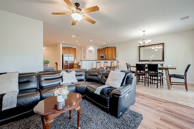 living room featuring a textured ceiling, ceiling fan with notable chandelier, and light wood-type flooring