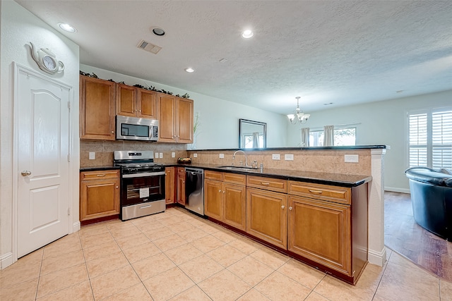 kitchen with kitchen peninsula, appliances with stainless steel finishes, sink, light tile patterned floors, and hanging light fixtures