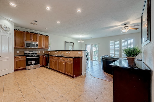 kitchen with sink, tasteful backsplash, kitchen peninsula, ceiling fan with notable chandelier, and appliances with stainless steel finishes