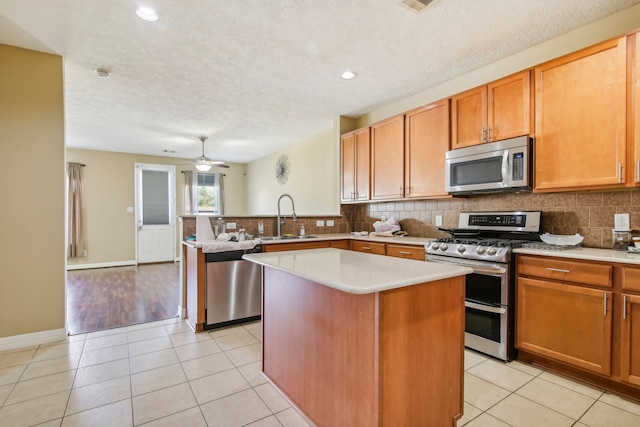 kitchen with sink, ceiling fan, light tile patterned floors, a kitchen island, and stainless steel appliances