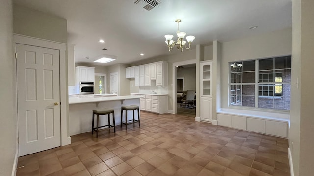 kitchen with kitchen peninsula, a breakfast bar, white cabinetry, a notable chandelier, and oven