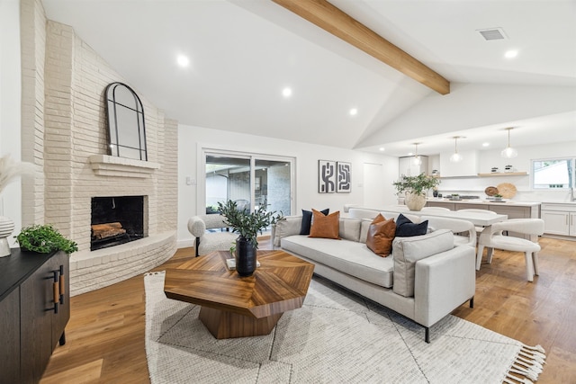 living room featuring a fireplace, beamed ceiling, light hardwood / wood-style floors, and high vaulted ceiling