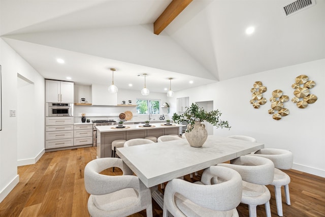 dining space featuring beam ceiling, high vaulted ceiling, light hardwood / wood-style flooring, and sink