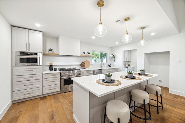 kitchen featuring a kitchen bar, light hardwood / wood-style flooring, pendant lighting, and appliances with stainless steel finishes