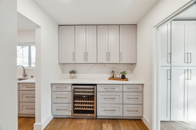 bar featuring decorative backsplash, light hardwood / wood-style floors, beverage cooler, and sink