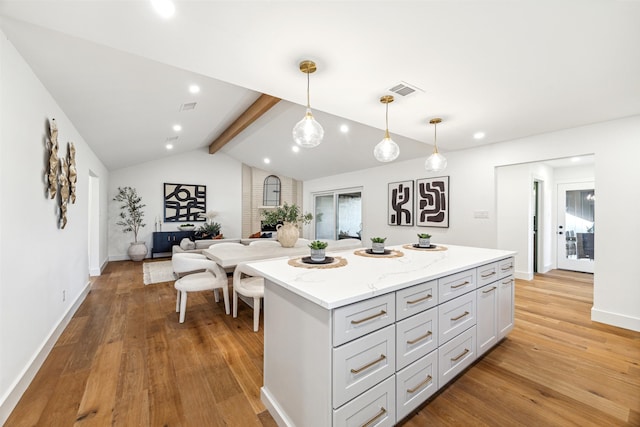 kitchen featuring pendant lighting, lofted ceiling with beams, a kitchen island, light stone countertops, and light hardwood / wood-style floors