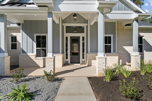 view of exterior entry with covered porch, brick siding, and board and batten siding