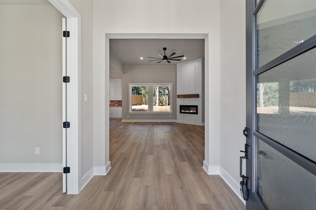 foyer entrance with a fireplace, wood finished floors, a ceiling fan, and baseboards