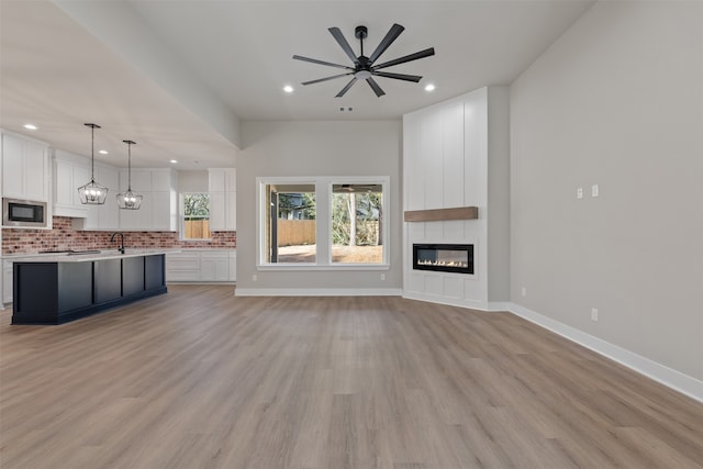 unfurnished living room featuring ceiling fan with notable chandelier, a large fireplace, light wood-type flooring, and sink