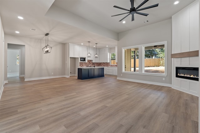 unfurnished living room with a ceiling fan, visible vents, a fireplace, and light wood-style flooring