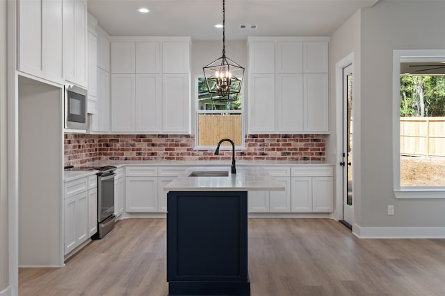 kitchen with white cabinetry, sink, stainless steel appliances, an island with sink, and decorative light fixtures