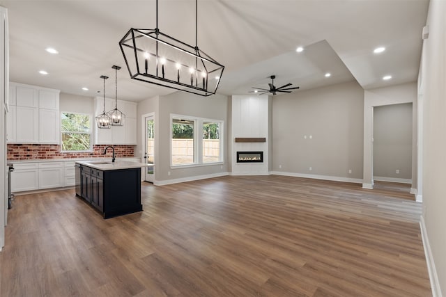 kitchen with ceiling fan, a large fireplace, hanging light fixtures, hardwood / wood-style floors, and a kitchen island with sink