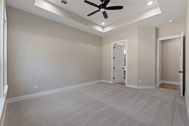 unfurnished bedroom featuring ceiling fan, light carpet, and a tray ceiling