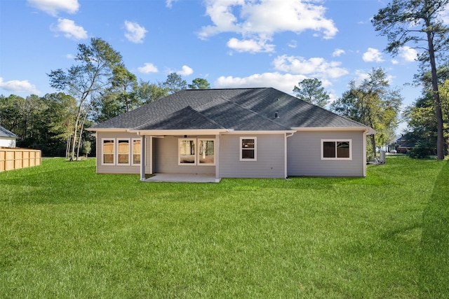 back of house with roof with shingles, a lawn, and a patio area