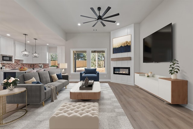 living area with a large fireplace, light wood-type flooring, baseboards, and recessed lighting