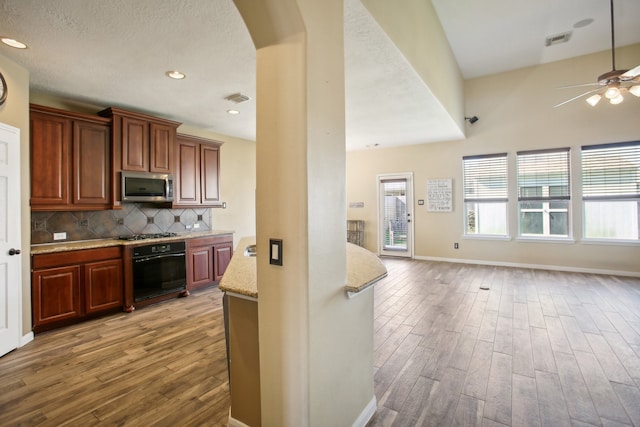 kitchen with decorative backsplash, light stone countertops, stainless steel appliances, ceiling fan, and light hardwood / wood-style floors