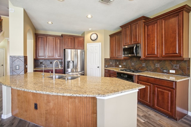 kitchen with decorative backsplash, appliances with stainless steel finishes, light stone counters, sink, and hardwood / wood-style flooring