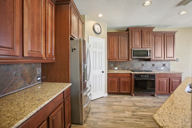 kitchen with tasteful backsplash, light stone counters, light hardwood / wood-style flooring, and appliances with stainless steel finishes