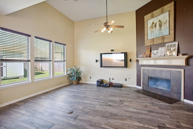 unfurnished living room featuring ceiling fan, wood-type flooring, high vaulted ceiling, and a tiled fireplace