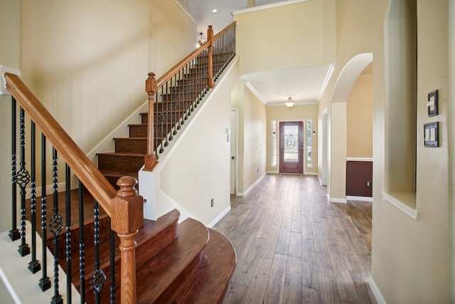 foyer entrance with hardwood / wood-style floors, ornamental molding, and a towering ceiling