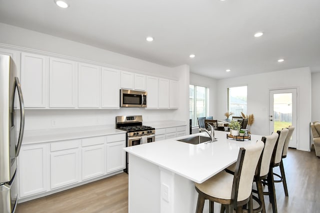 kitchen with white cabinets, stainless steel appliances, light hardwood / wood-style flooring, and a center island with sink