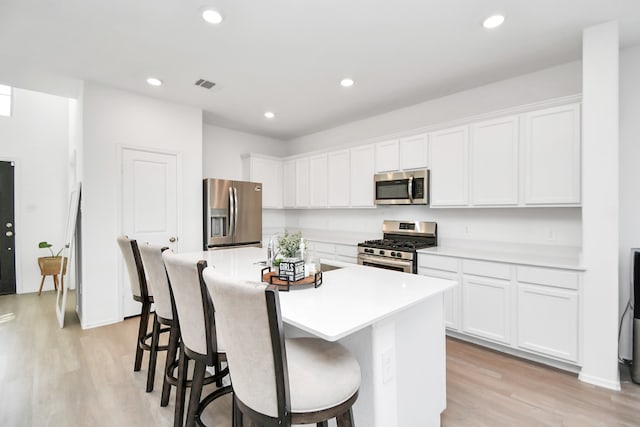 kitchen featuring white cabinets, a center island with sink, stainless steel appliances, and light hardwood / wood-style flooring