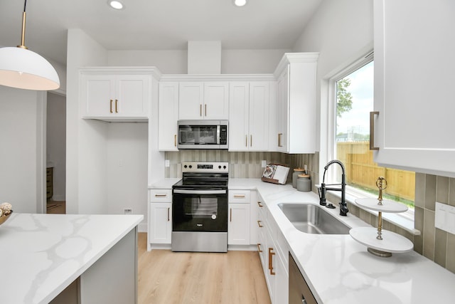 kitchen featuring white cabinets, hanging light fixtures, sink, light stone countertops, and appliances with stainless steel finishes