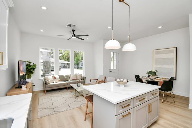 kitchen with pendant lighting, a center island, ceiling fan, light stone counters, and a kitchen bar