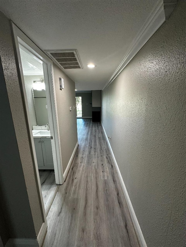 hall featuring a textured ceiling, sink, light wood-type flooring, and crown molding