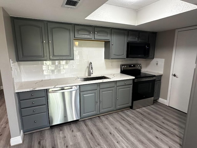 kitchen with appliances with stainless steel finishes, light hardwood / wood-style floors, gray cabinetry, and sink