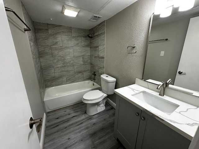 full bathroom featuring a textured ceiling, vanity, tiled shower / bath combo, hardwood / wood-style flooring, and toilet