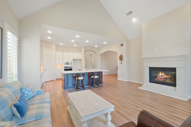 living room featuring high vaulted ceiling, light hardwood / wood-style flooring, and sink