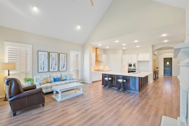 living room with sink, high vaulted ceiling, and light wood-type flooring