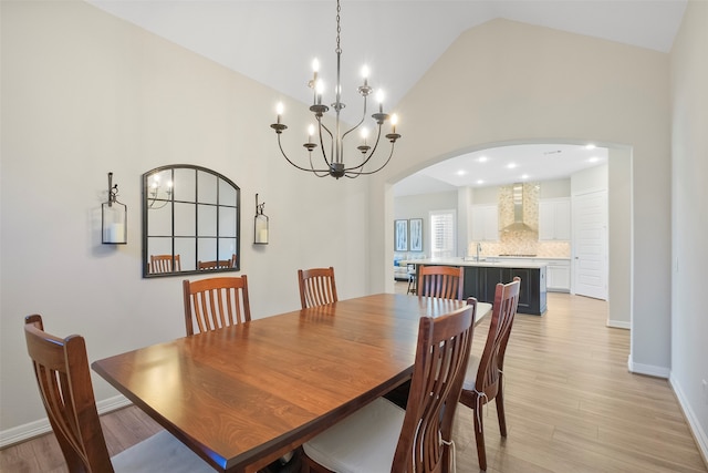 dining area featuring light wood-type flooring, high vaulted ceiling, a notable chandelier, and sink