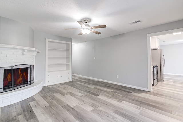 unfurnished living room with ceiling fan, light wood-type flooring, a textured ceiling, and a brick fireplace