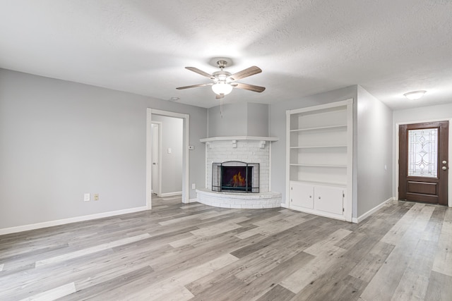 unfurnished living room featuring light wood-type flooring, a brick fireplace, a textured ceiling, ceiling fan, and built in features