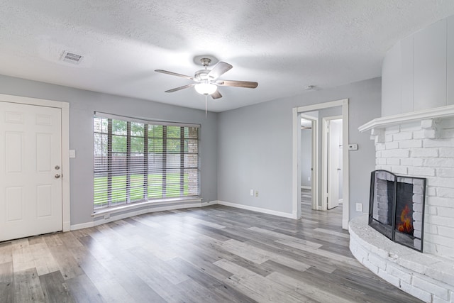 unfurnished living room with a textured ceiling, light hardwood / wood-style floors, a brick fireplace, and ceiling fan