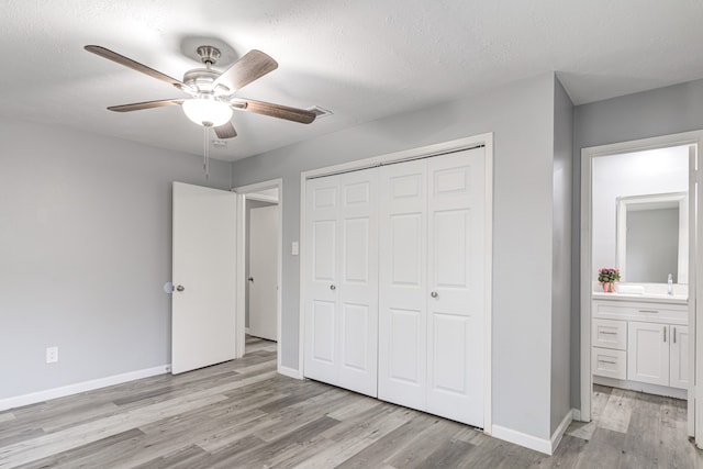 unfurnished bedroom featuring ceiling fan, ensuite bathroom, a textured ceiling, and light wood-type flooring