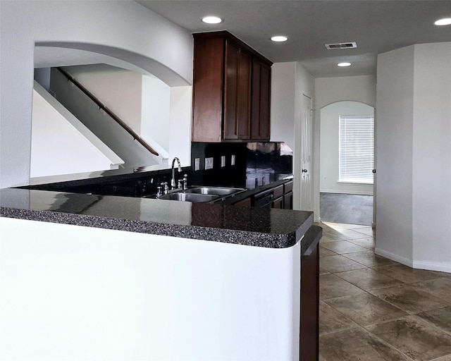 kitchen with dark tile patterned floors, dark brown cabinetry, kitchen peninsula, and sink