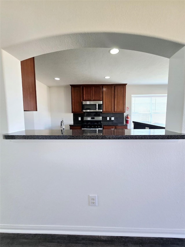 kitchen featuring dark stone countertops, kitchen peninsula, and stainless steel appliances