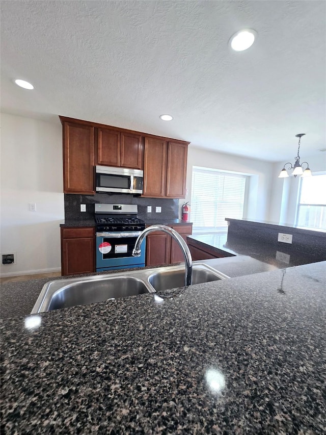 kitchen featuring decorative backsplash, appliances with stainless steel finishes, dark stone counters, an inviting chandelier, and hanging light fixtures